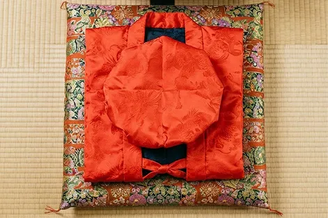 畳に置かれた長寿祝い用の赤いちゃんちゃんこ。美しい刺繍が施された座布団と共に、ハレの日の特別な演出として大切に整えられています。
