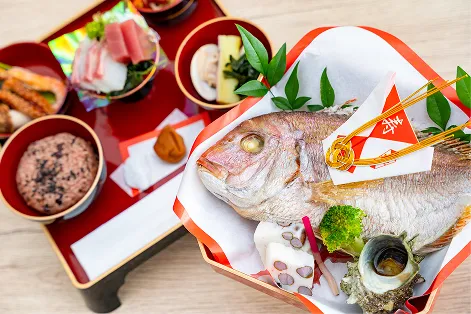 お子様の成長を願う本格的なお食い初め膳。縁起の良い尾頭付きの焼き鯛を中心に、お赤飯、お造り、煮物などが、格式高い赤漆塗りのお膳に美しく整えられています。