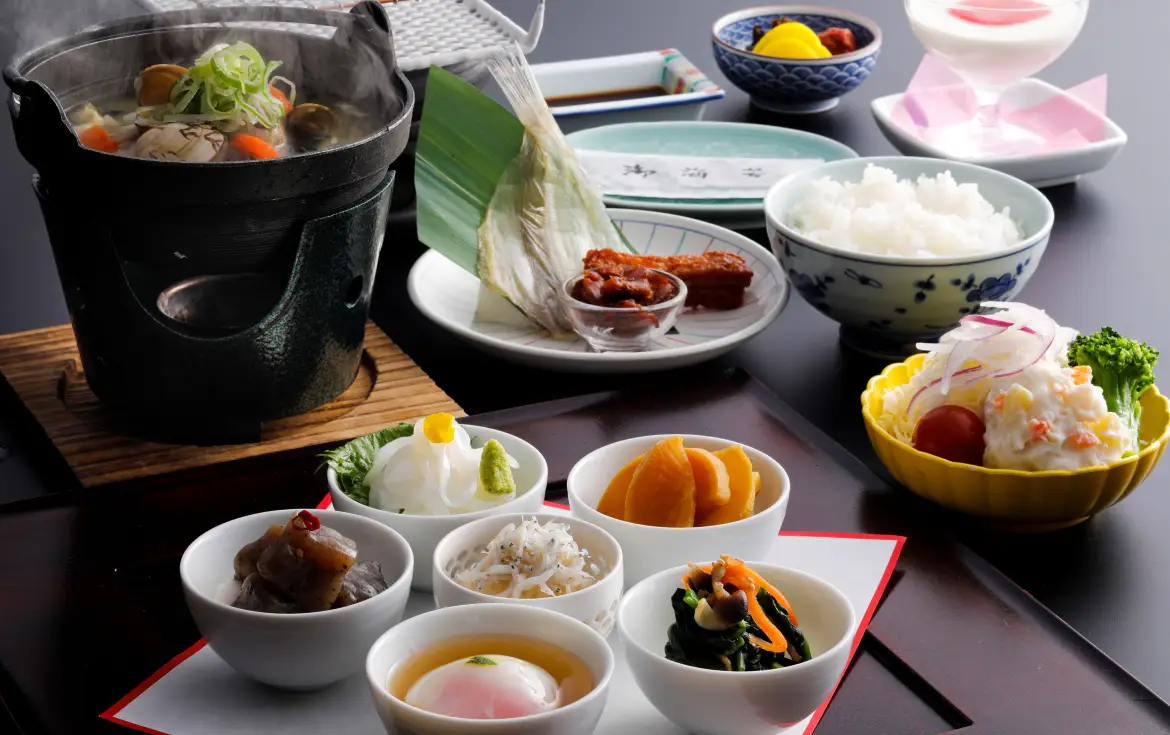 湯気が立ち上る小鍋と、温泉卵や小鉢がバランスよく並んだ温かみのある朝食和定食。