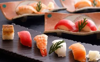黒い角皿や和食器に美しく盛り付けられた、マグロ、エビ、サーモンなどの握り寿司。