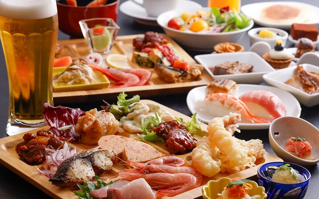 盛り付けられた多彩なビュッフェ料理と生ビール。天麩羅、刺身、寿司からスイーツまで揃った賑やかな食卓。