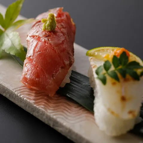 細かな飾り包丁が施されたマグロと、柑橘を添えた白身の握り寿司。素材の瑞々しさが際立つ一皿。