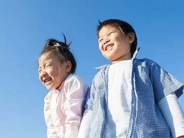 青空を背景に、満面の笑みで並ぶ男の子と女の子。