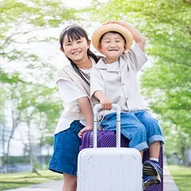 スーツケースにまたがって笑顔を見せる男の子と、隣に立つ女の子。