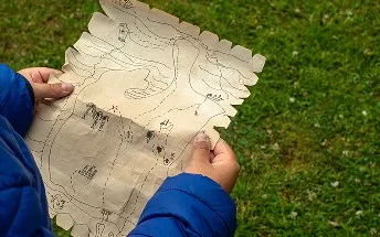 古びた宝地図のようなデザインのマップを広げ、冒険に胸を躍らせる子供の手元の様子。