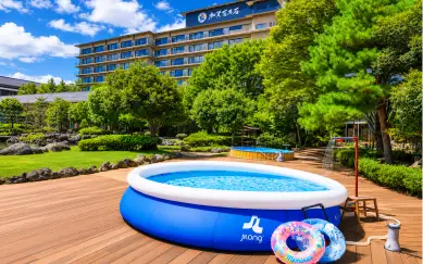 青空のもと、ホテルの庭園のウッドデッキに設置された大きな家庭用ビニールプールと浮き輪。
