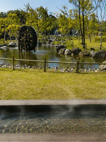 湯気が立ち上る足湯テラスから望む日本庭園と大きな木製水車