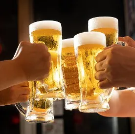 黄金色のビールが注がれたジョッキを掲げ、数名で賑やかに乾杯をする手元のアップ。