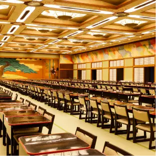 松の舞台がある大広間に、会議や研修に適した4人掛けのテーブル席が配置されている様子。