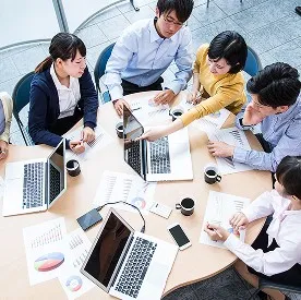 円卓を囲んで資料やパソコンを広げ、打ち合わせをするグループの様子。