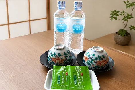 木製テーブルの上に用意された、2本のペットボトル水と湯呑み、緑茶のティーバッグ。