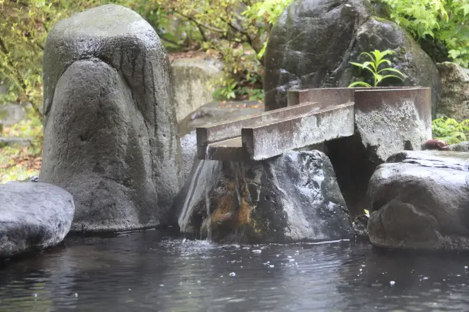庭園の岩の間から筧（かけひ）を通じて源泉が注ぎ込まれる、風情ある湯口の様子。