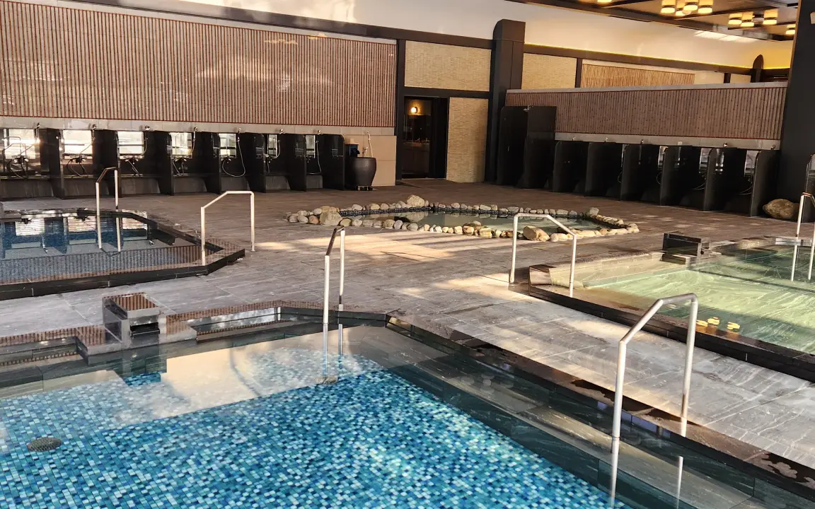 グレーの石造りの床に複数の浴槽が並ぶ、広々とした本館大浴場「加賀浴殿」の様子。