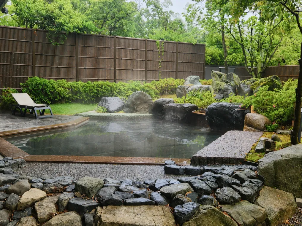 竹垣と豊かな緑に囲まれた、岩造りの情緒ある露天風呂の風景。