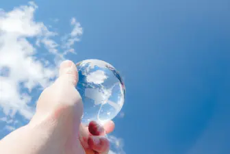 青空を背景に透明な地球儀を掲げる手のイメージ